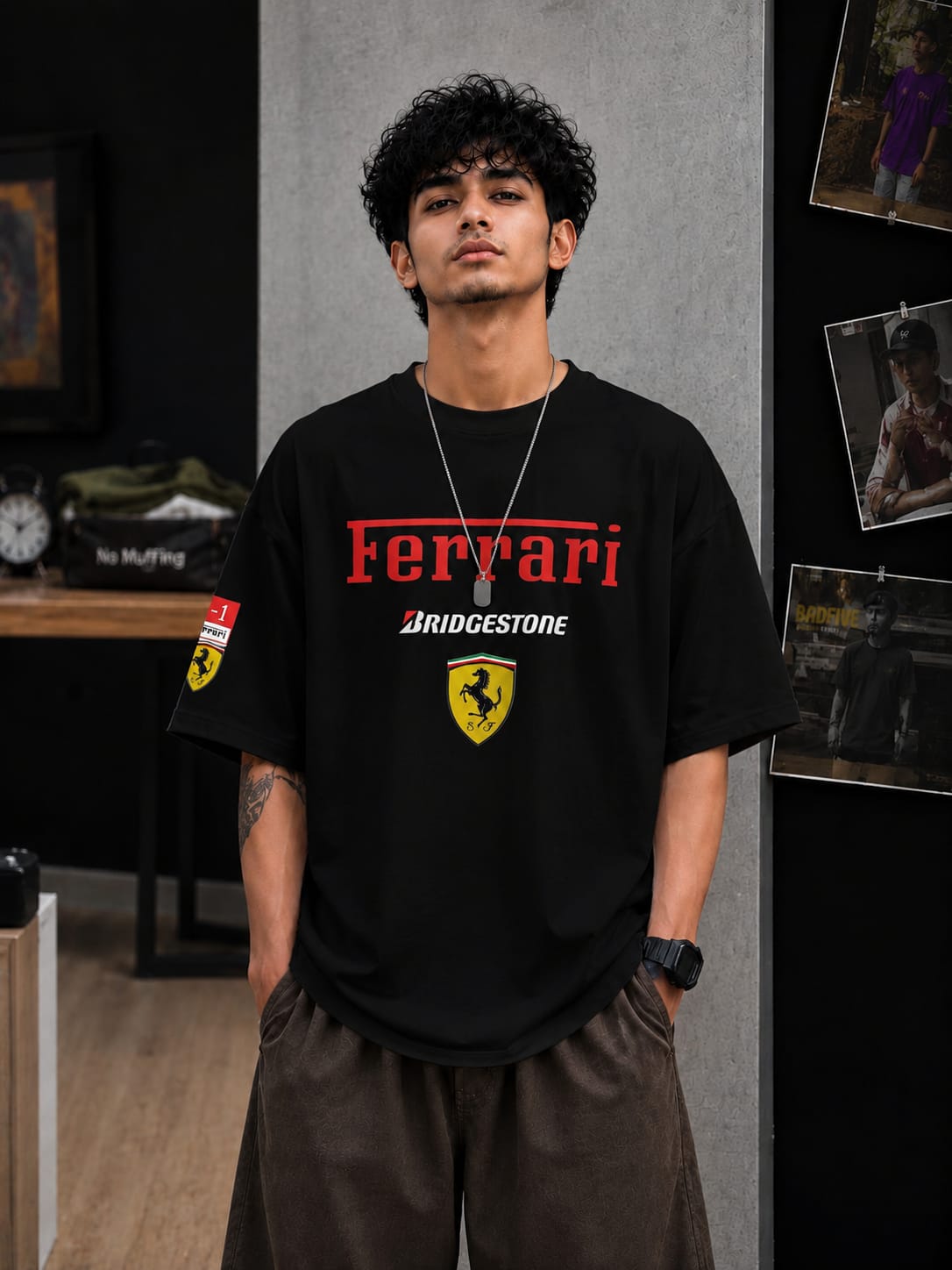 A man wearing a black Ferrari t-shirt with red and white branding and a yellow shield logo, paired with brown pants, standing in a styled indoor setting.